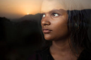 Serene girl looking at sunset view from behind glass window.